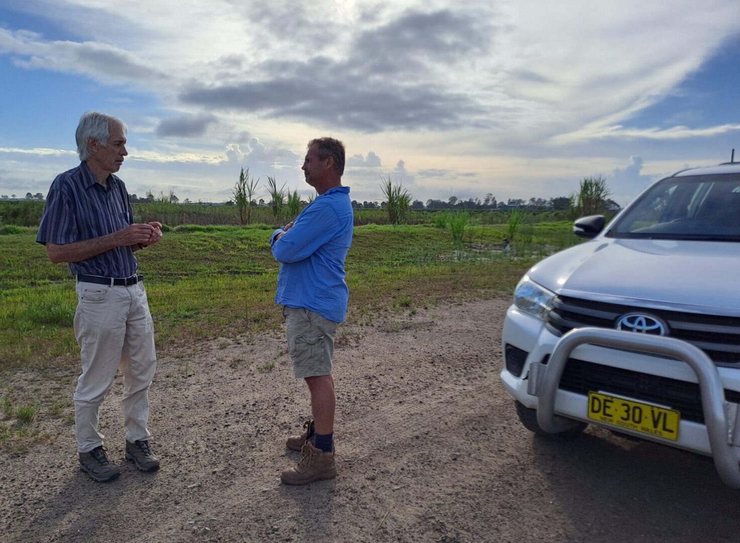 Two men standing next to a white car.